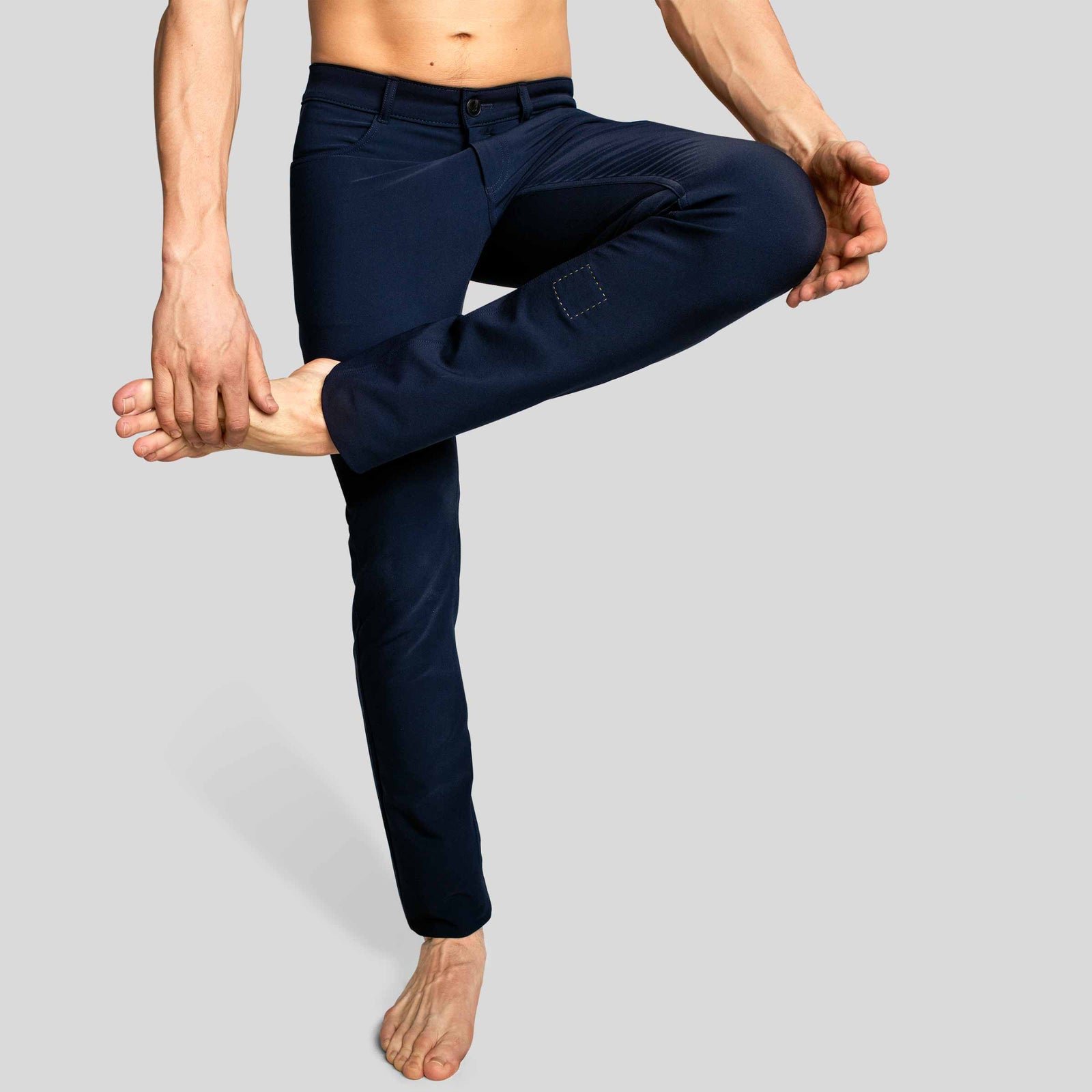 A man standing with the one leg crossed, wearing åäö’s The Pants in Blue Black, showcasing their flexibility and refined fit.”