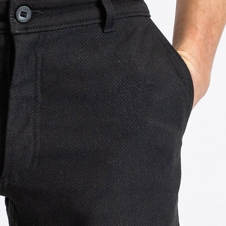 Close-up of a man in åäö’s Forever Pants, hand in pocket, highlighting the Dyneema fabric texture and a reinforced button.