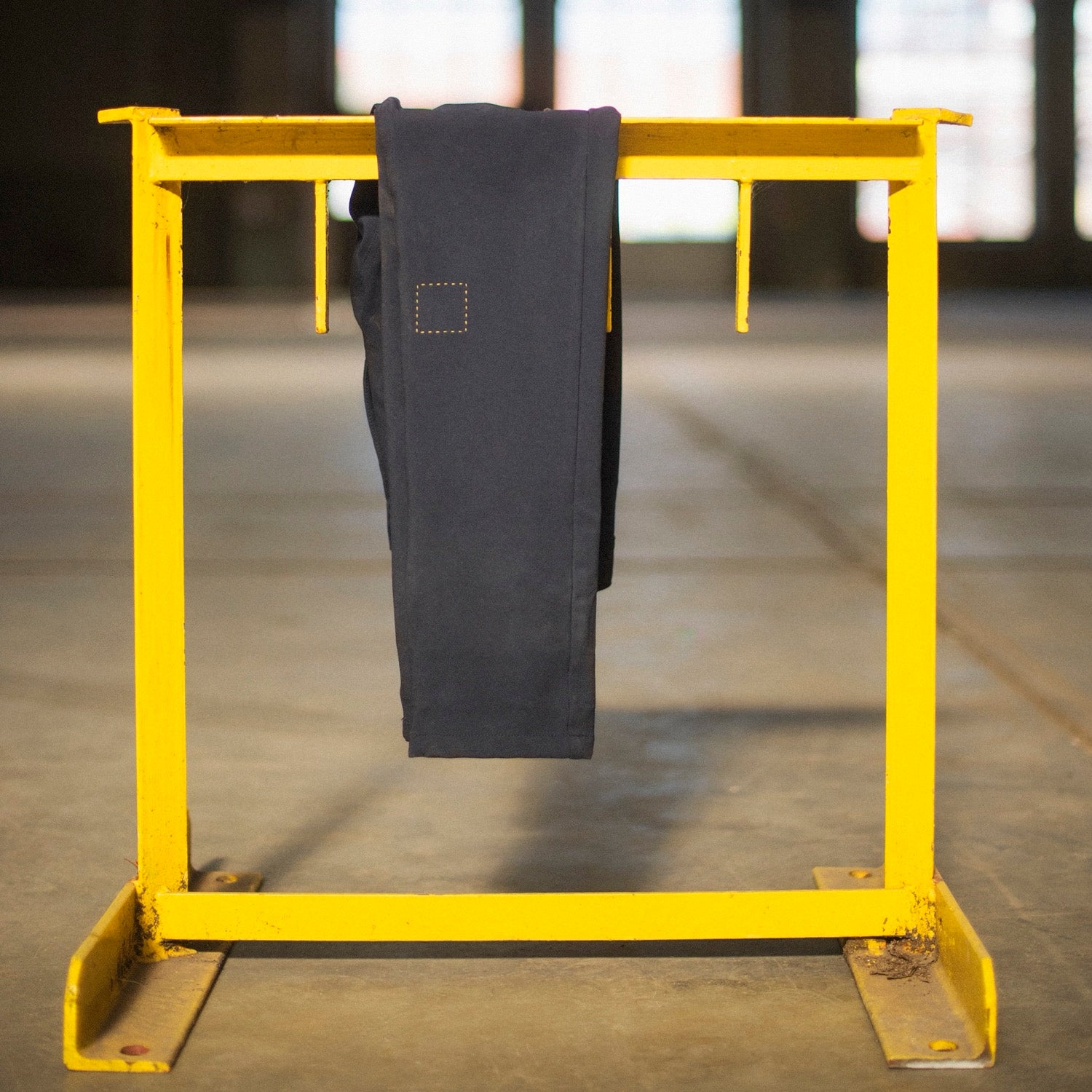 Yellow metal frame with a pair of The Pants by åäö hanging on it against a blurred background