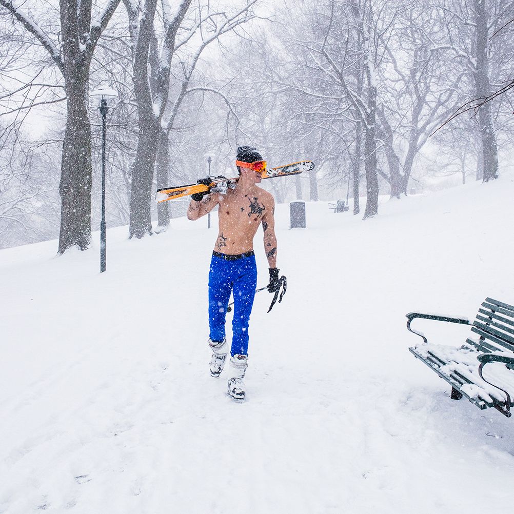 A man walking shirtless in a snowy park, wearing åäö’s The Pants in Brilliant Blue with skis over his shoulder.