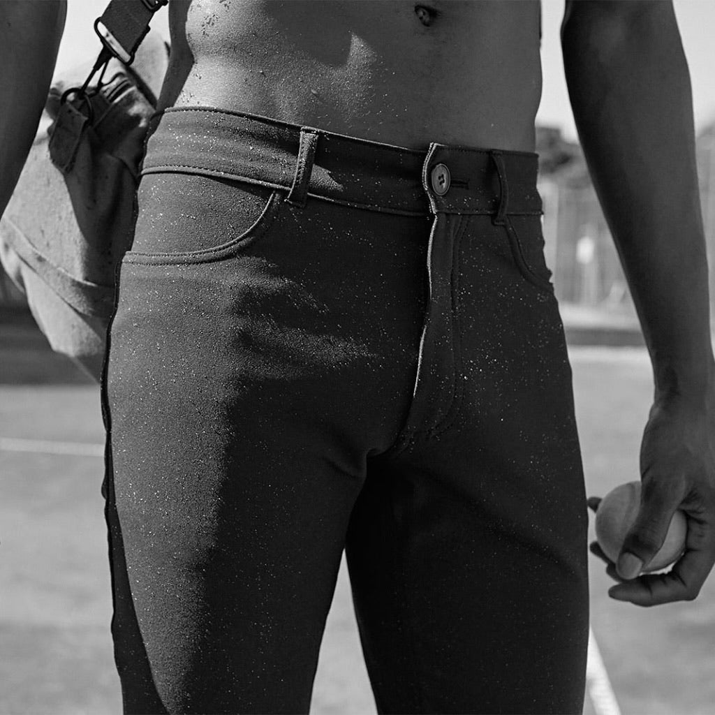 Black-and-white close-up of a man in åäö’s Blue Black Pants with water droplets, highlighting the water-repellent fabric.