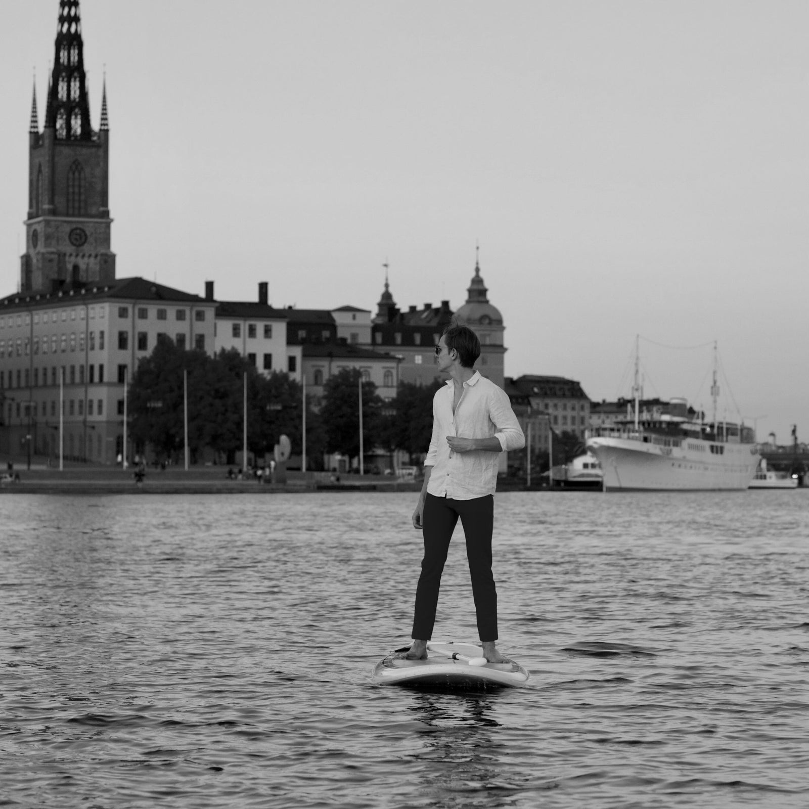 Man on paddle board wearing The Pants by åäö with a Stockholm cityscape in the background