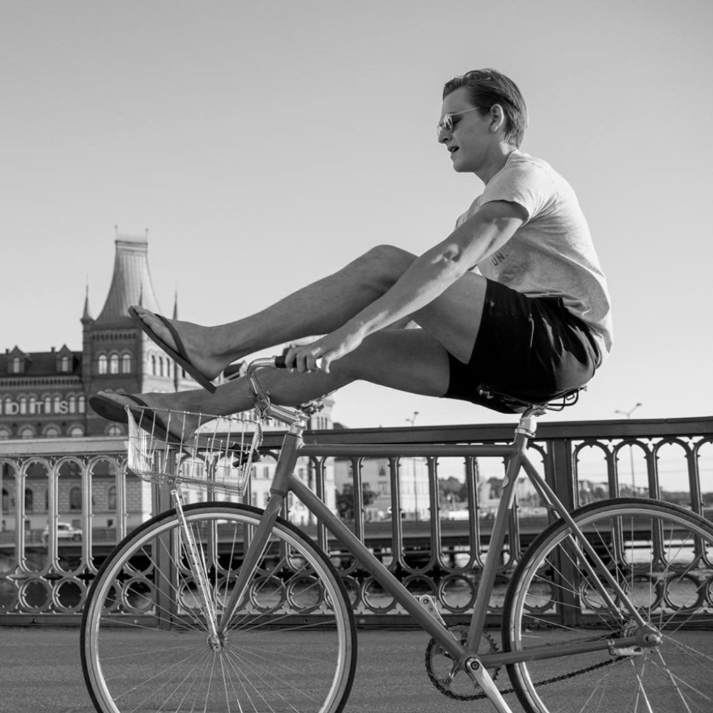 A black-and-white image of a man wearing åäö’s Deep Blue Shorts, sitting on a bike with his legs resting on the handlebars.