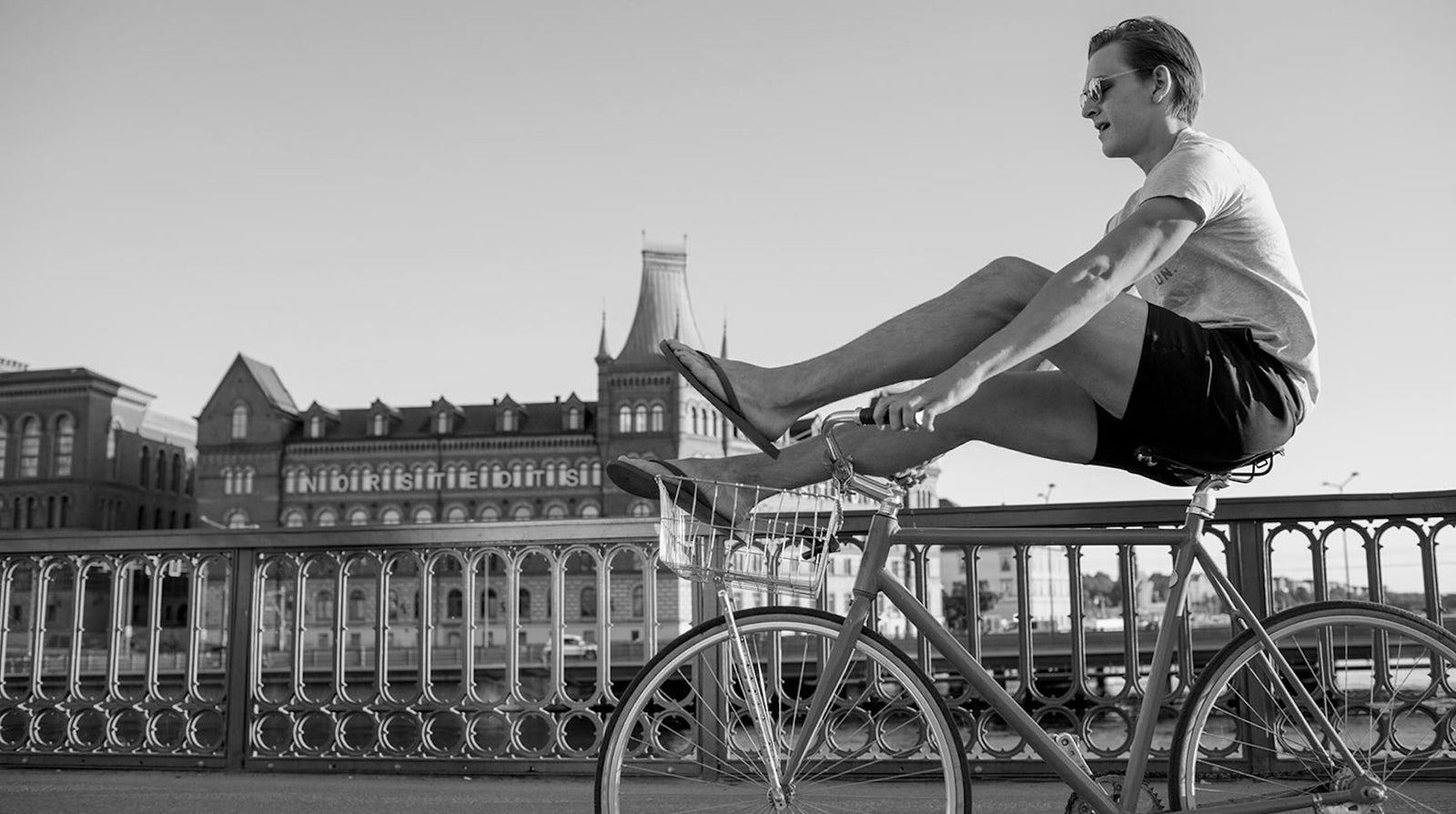 A black-and-white image of a man wearing åäö’s Deep Blue Shorts, sitting on a bike with his legs resting on the handlebars.