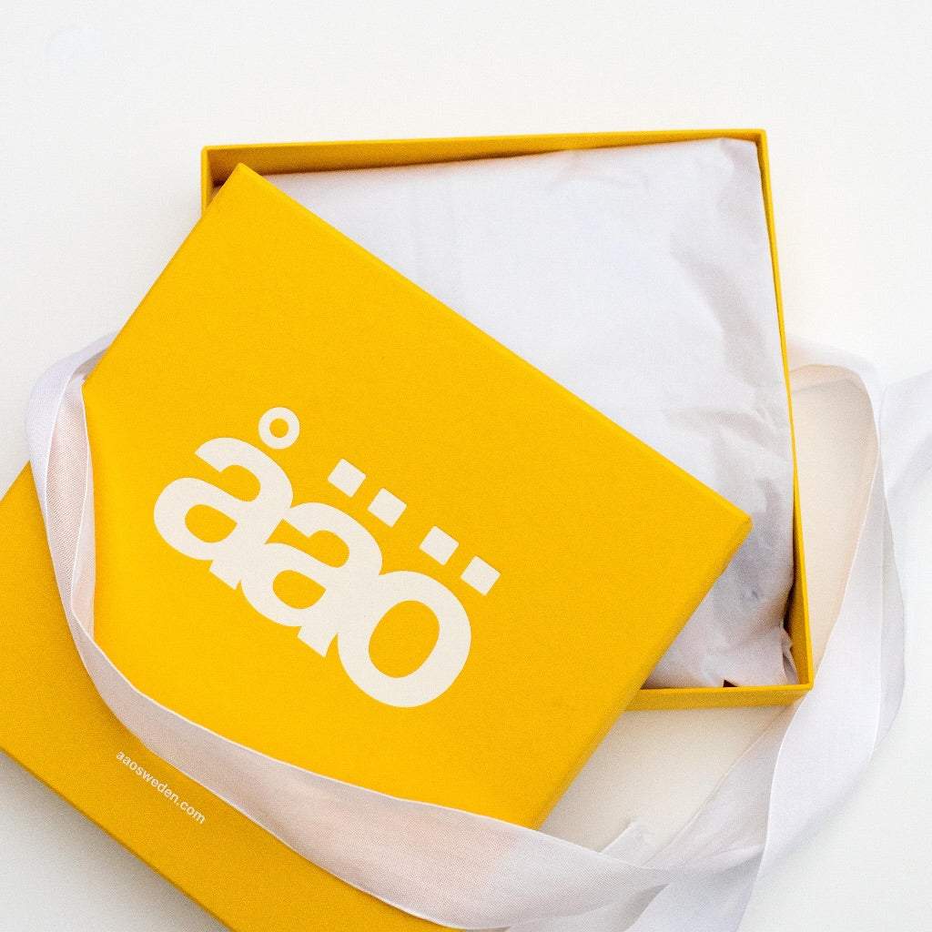 A vibrant yellow åäö product box with the logo printed on it, lined with silk paper inside for an elegant touch.