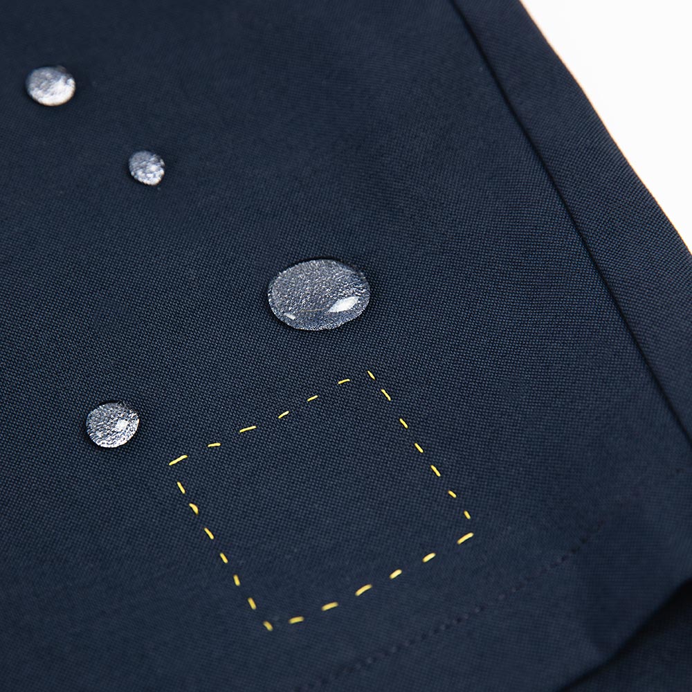 Close-up of water forming four droplets on the fabric of åäö’s Shorts, showing the precision-crafted water-repellent material