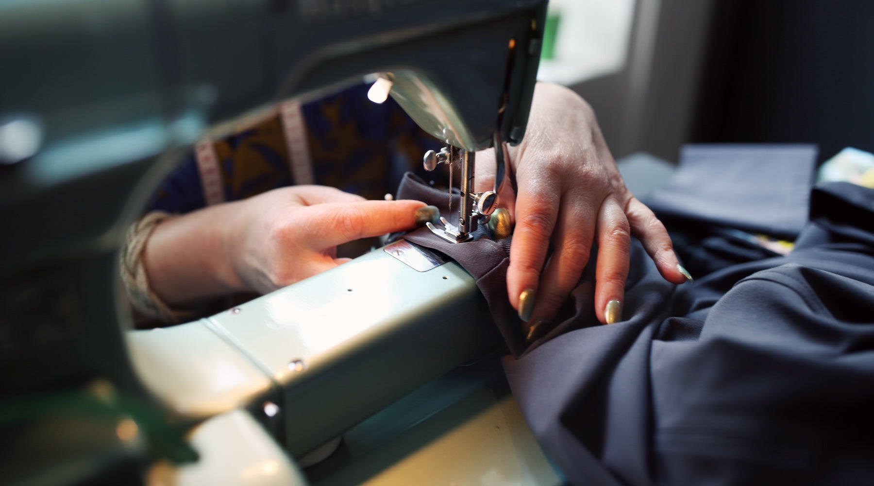 A seamstress hemming åäö’s The Pants on a sewing machine, highlighting meticulous craftsmanship and attention to detail.