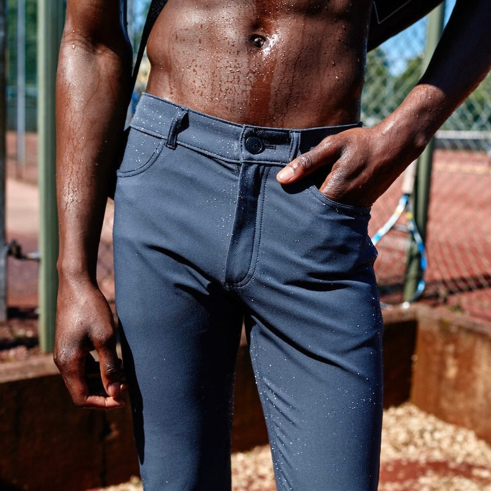 A man wearing The Pants by åäö in Tech Black on a tennis court, highlighting the meticulous stitching and sleek waistband design.