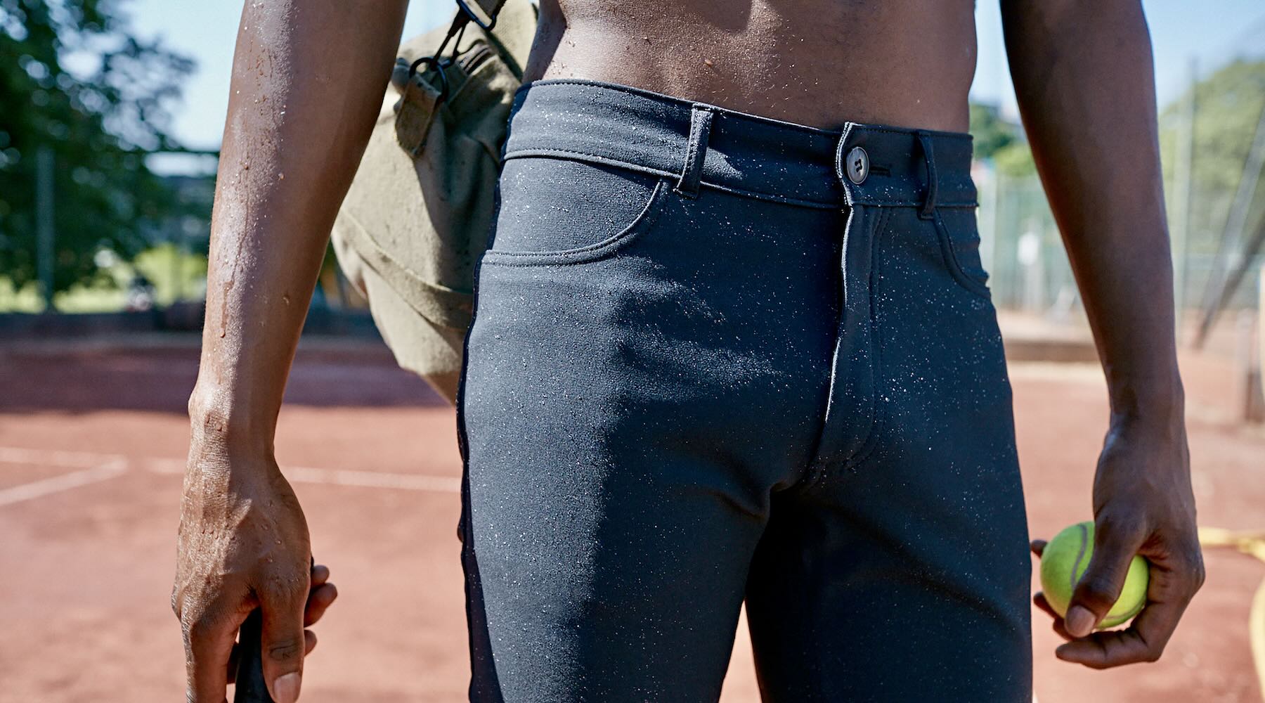 A man wearing The Pants by åäö in Tech Black on a tennis court, highlighting the meticulous stitching and sleek waistband design.