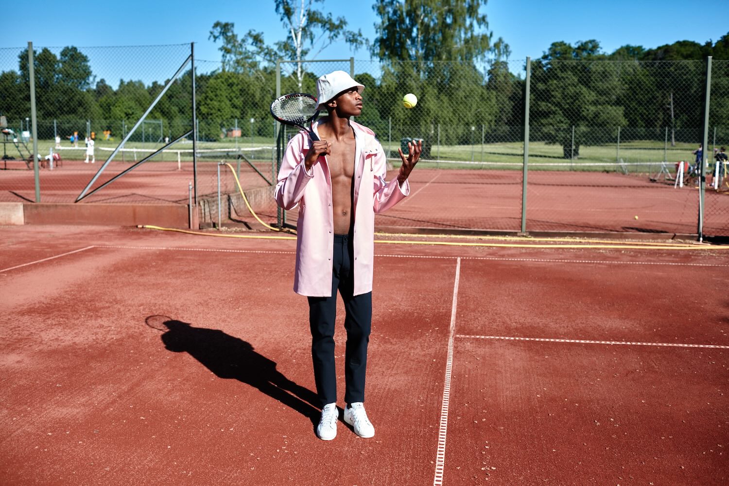 A man standing on a tennis court in The Pants by åäö in Tech Black, throwing a tennis ball, showcasing their versatile design.