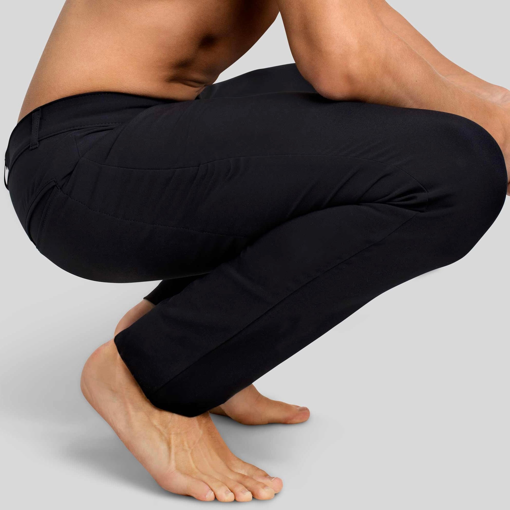 A man squatting in åäö’s The Pants in Tech Black, showcasing their tailored fit and functional design